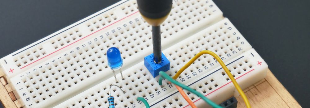 example components of a miniature LED light kit for book nooks showing the electronic broadboard with LED bulb, resistor wire and the potentiometer being adjusted to change voltage.