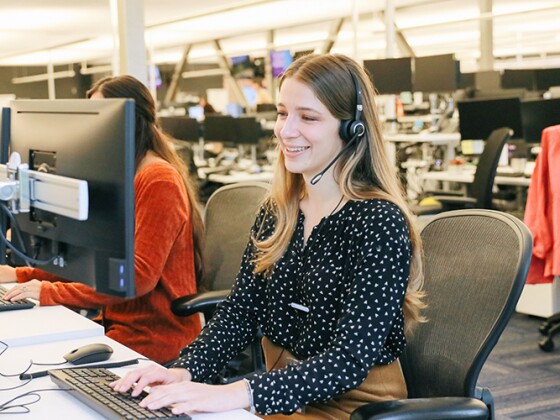 Image of woman in an office with headset on looking at computer helping customers