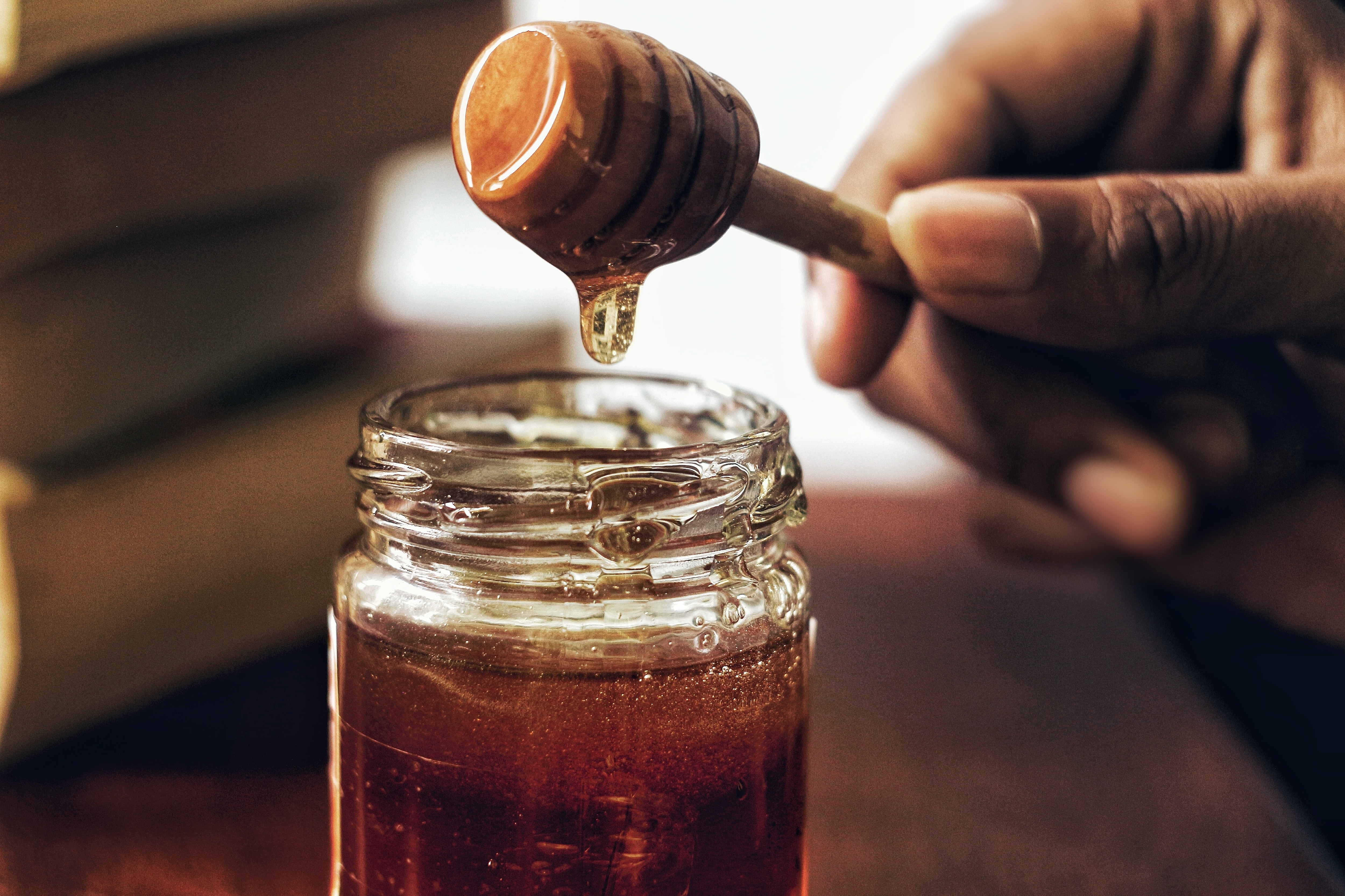 Hand holding honey dripper above jar of honey