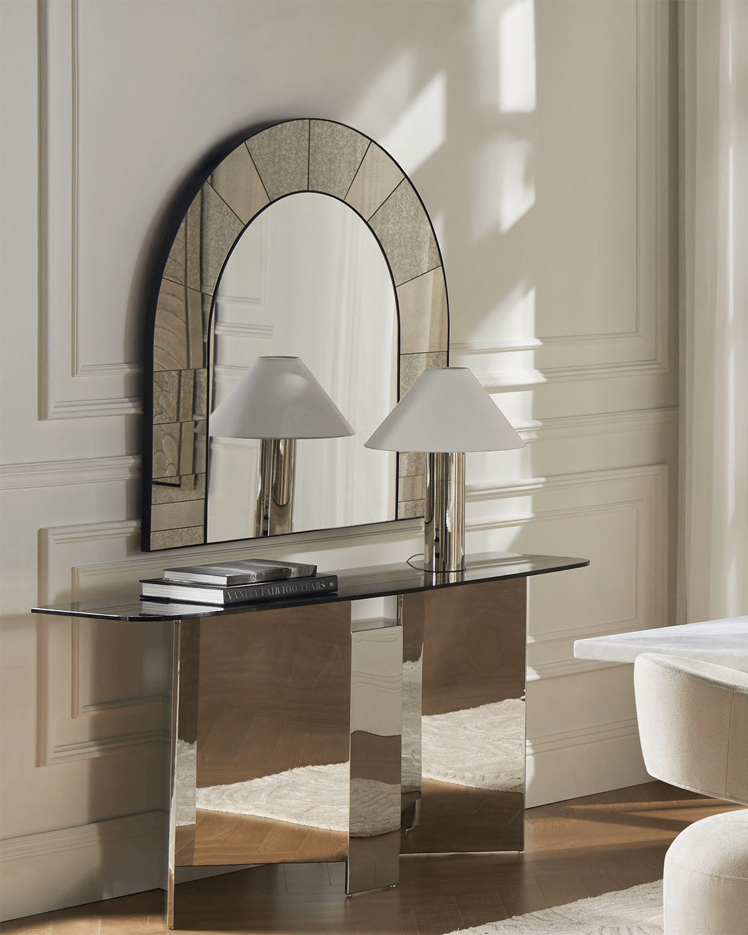 Refined modern space featuring a Z Gallerie mirror with an arched silhouette and tiled-look border, leaning against a paneled wall. Styled with a sleek mirrored console table, stacked design books, and a contemporary chrome lamp, the setting reflects clean lines, soft light, and elevated minimalism.