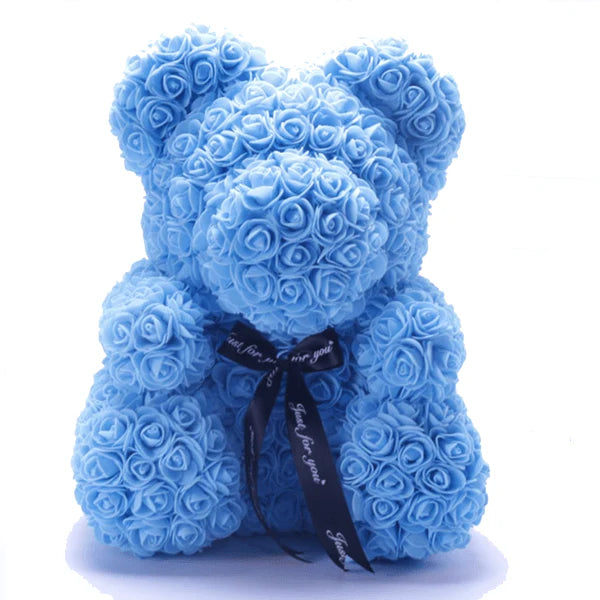 A teddy bear formed from light blue artificial roses, adorned with a black ribbon printed with white text.
