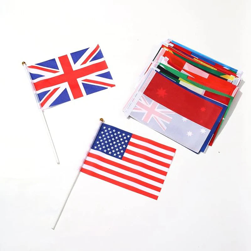 Miniature UK and USA flags on white sticks next to a stack of folded assorted international flags on a white background.