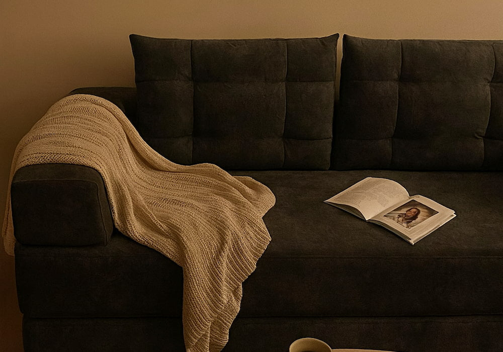 Sofa bed with a beige throw blanket and an open book, showcasing a cozy and versatile living room space.